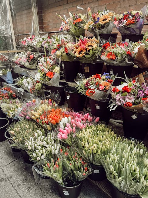 A display of freshly arranged flower bouquets at a florist shop, featuring a variety of colourful blooms including pink tulips, orange roses, purple irises, white lilies, and red anemones, all wrapped